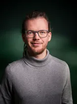 Arno Meuter, Halbportrait, lächelnd, Blick in Kamera, dunkelgrüner Hintergrund