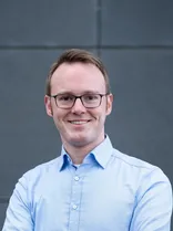 Bastian Schneider, Halbportrait, lächelnd, Blick in Kamera, neutraler Hintergrund