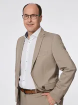 Michael Kolb, formelles Halbporträt, lächelnd, Blick in Kamera, neutraler Hintergrund