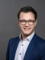 Robin Schuster, Halbportrait, lächelnd, Blick in Kamera, neutraler Hintergrund