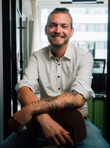 Yannick Veits, lächelnd, tätowierter Arm, Blick in Kamera, Büro im Hintergrund