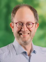 Chris Rihm, Halbportrait, lächelnd, Blick in Kamera, grüner Hintergrund