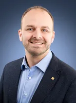 Andreas Renner, Halbportrait, lächelnd, Blick in Kamera, blauer Hintergrund