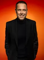 Frank Ortolf, Halbportrait, lächelnd, Blick in Kamera, roter Hintergrund