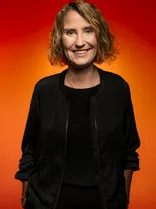 Bettina Fischer, Halbportrait, lächelnd, Blick in Kamera, roter Hintergrund