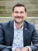 Daniel Karrais, formelles Halbporträt, lächelnd, Blick in Kamera, draußen