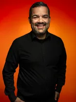 Danny Multani, Halbportrait, lächelnd, Blick in Kamera, roter Hintergrund