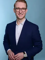 Lennart Christ, Halbportrait, lächelnd, Blick in Kamera, blauer Hintergrund