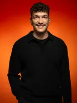 Yannik Hummel, Portrait, lächelnd, Blick in Kamera, roter Hintergrund
